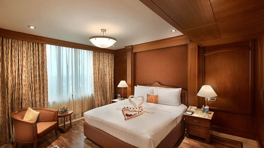 A hotel room with wooden interiors, a plush bed, bedside lamps, and elegant drapes at Accord Metropolitan.