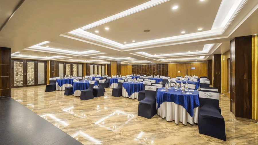 Banquet hall at The Citrine, Bangalore, arranged cluster-style with round tables in blue cloths, branded chairs, and decorative coffered ceiling.