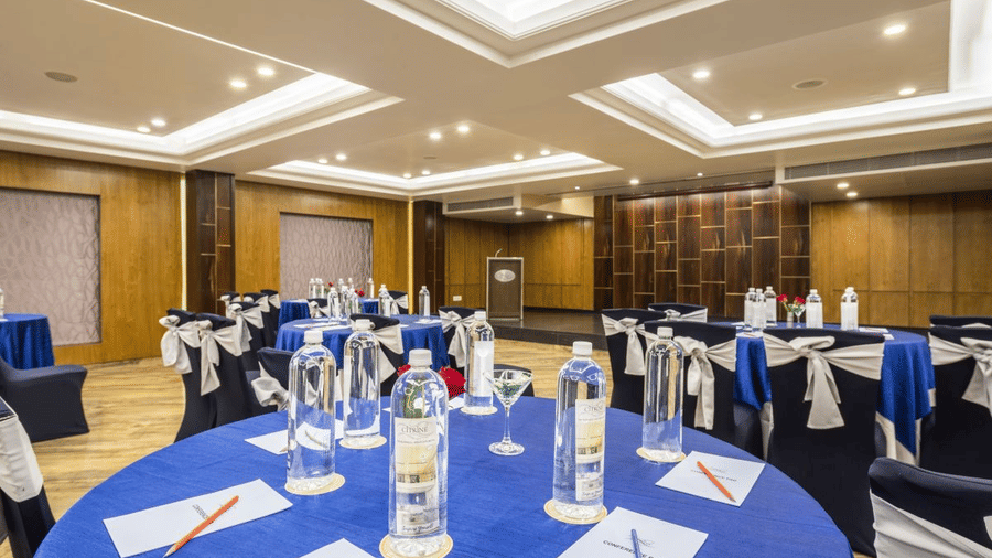 Banquet hall at The Citrine, Bangalore, arranged with round tables in blue cloths, water bottles, conference pads, and chairs with branded sashes.