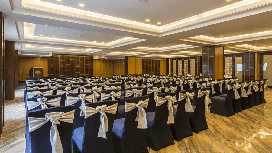 Banquet hall at The Citrine, Bangalore, set theatre-style with black chairs tied with silver sash bows under a coffered illuminated ceiling.