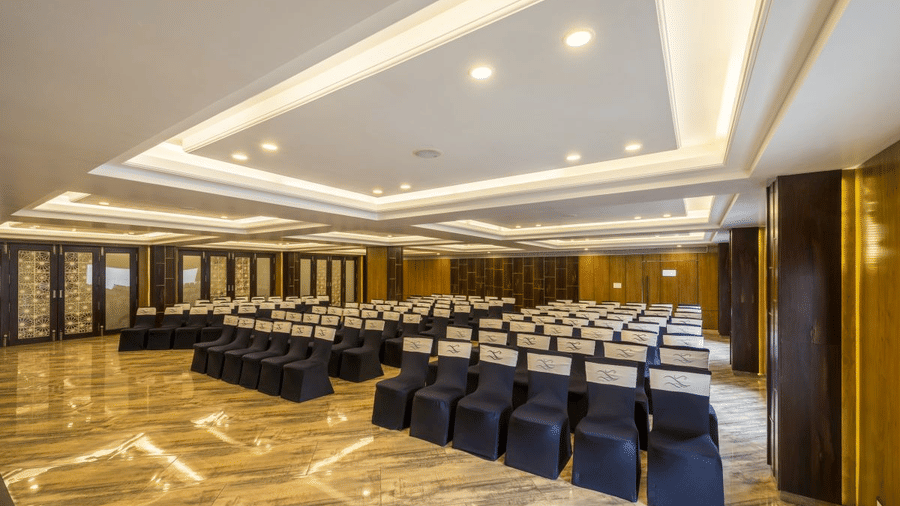 Banquet hall at The Citrine, Bangalore, set theatre-style with rows of black chairs facing a wood-panelled wall under a coffered ceiling.