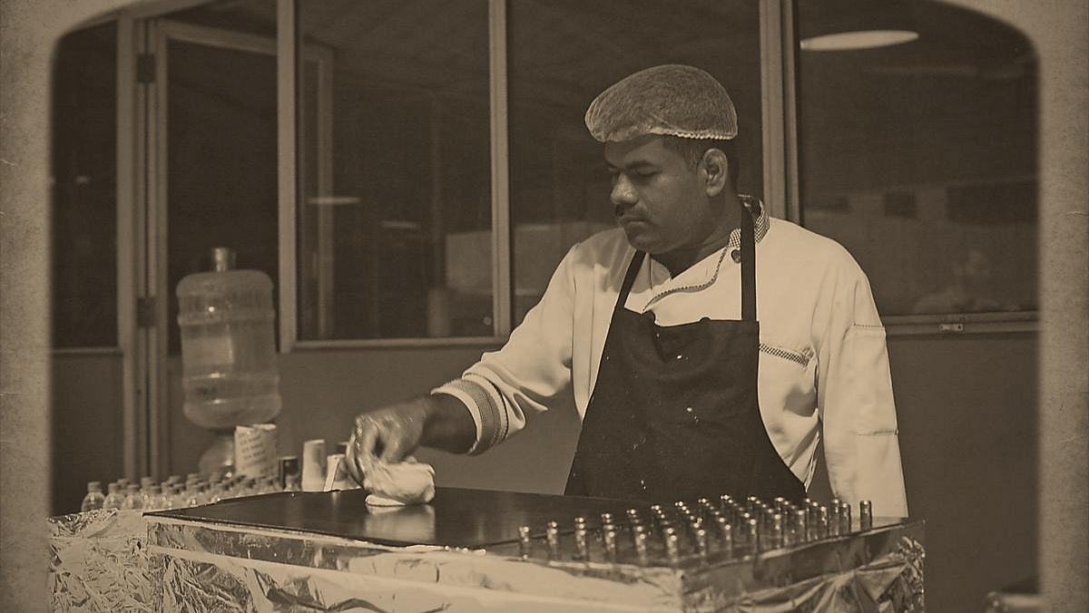 Black and white photo of a chef in an apron cooking on a grill.