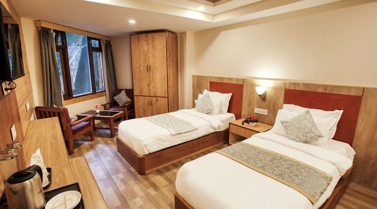 Standard Twin Room at Avianna Gangtok Prime Hotel & Spa featuring a couple of twin beds facing the TV mounted on the wall below which is tea and coffee maker. On one side of the bed is a sitting space next to the window