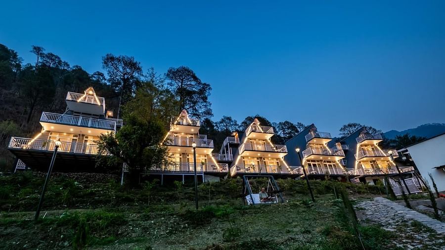 A panoramic view of several illuminated A-frame cottages at dusk, nestled on a hillside with surrounding trees.