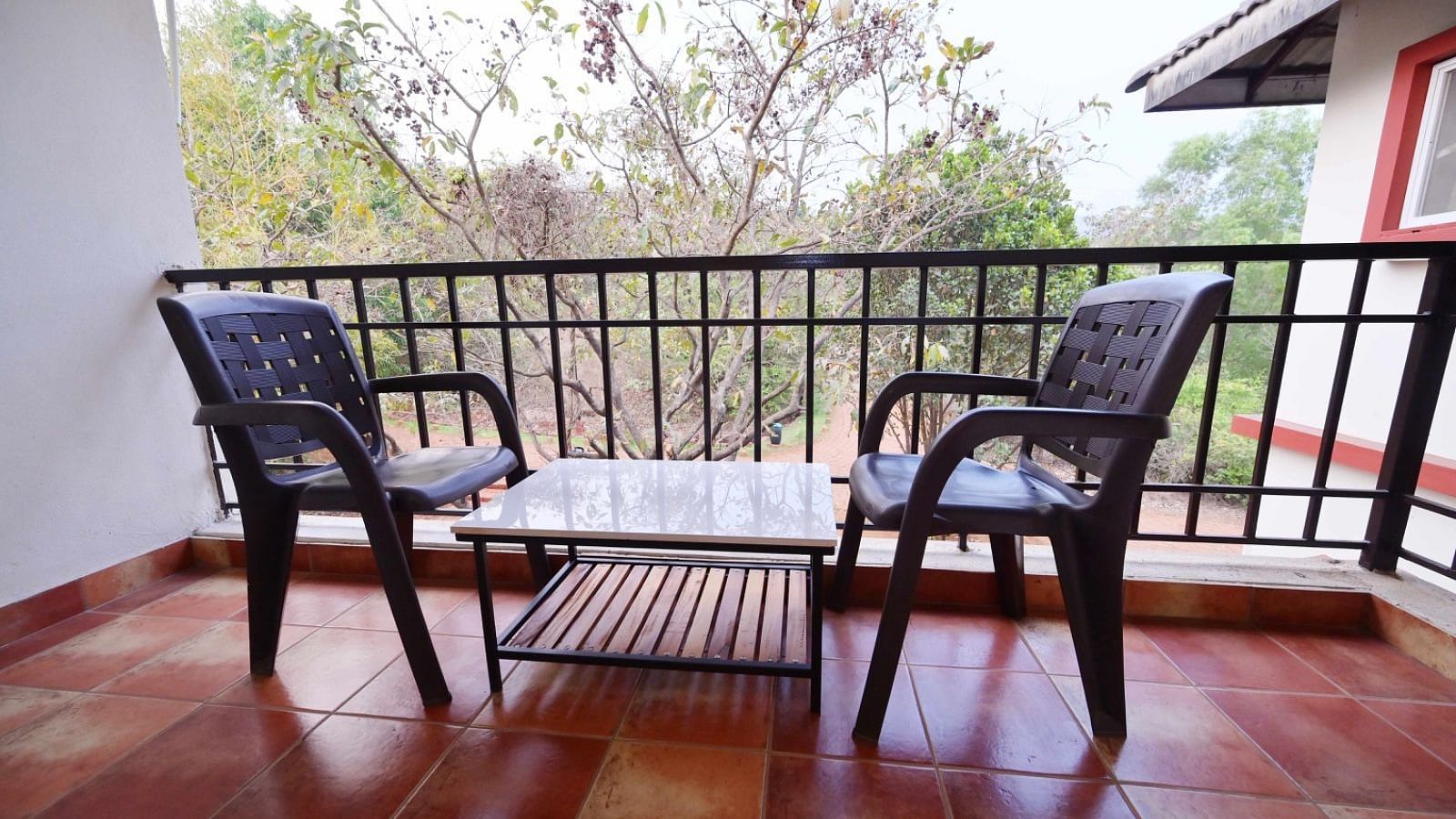 Balcony with two dark chairs, a small table, and a view of trees and a building.