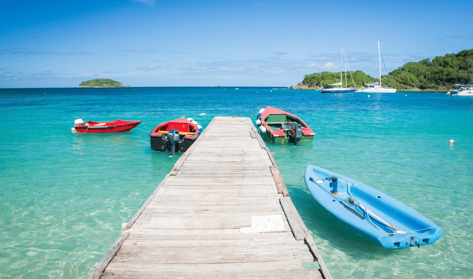 A long shot of a beach with a woodden bridge in between with boats on either side.