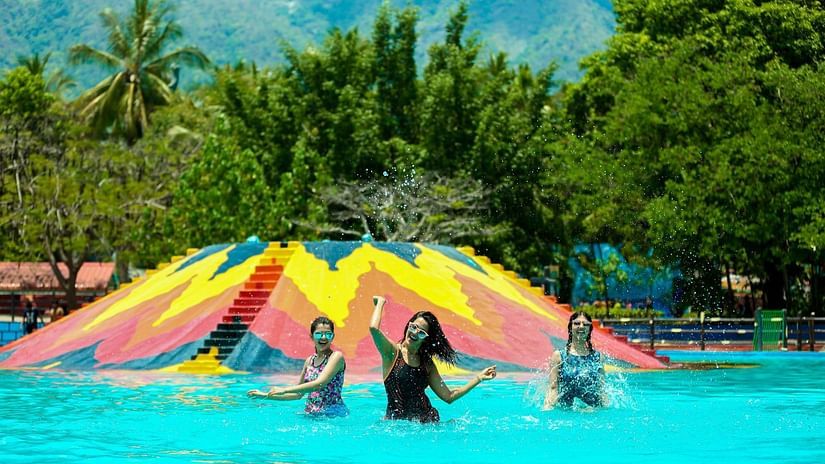 People splashing and enjoying in a swimming pool at Black Thunder surrounded by lush green trees in the background