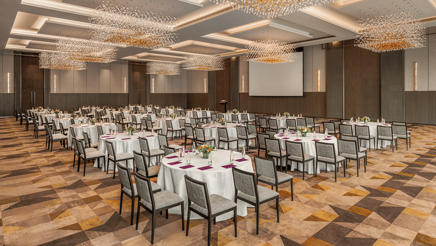 An expansive banquet hall of Ballroom 1 arranged in a conference setup featuring round dining tables with white tablecloths under geometric illuminated ceiling panels at The Residency Towers Chennai.