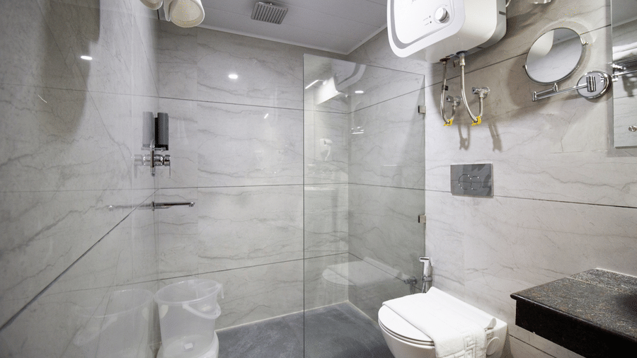 A glass shower enclosure, a toilet, a wall mirror, and a water heater in a hotel bathroom at Valmere Lungta Boutique Hotel & Spa, Darjeeling.