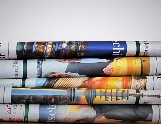View of a stack of rolled-up newspapers with various headlines and images.