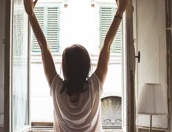 View of a Woman from the back stretching by a large window, enjoying the morning light.