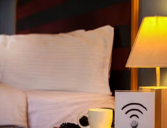 View of a cosy hotel bed with warm lighting and a Wi-Fi sign on the nightstand.