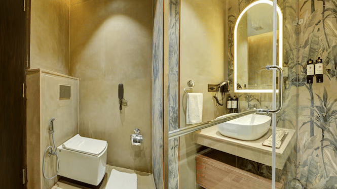 A collage featuring different angles of the bathroom at the Standard Room showcasing a commode, a wash basin along with a back-lit mirror above it at Hotel 91 Privé, Gurugram.
