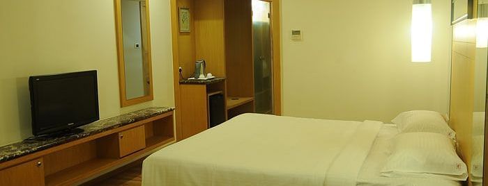 A modern hotel room with a neatly made bed, flat-screen TV, and soft lighting, ensuring a comfortable stay.- Dhanalakshmi Srinivasan Hotels, Perambalur