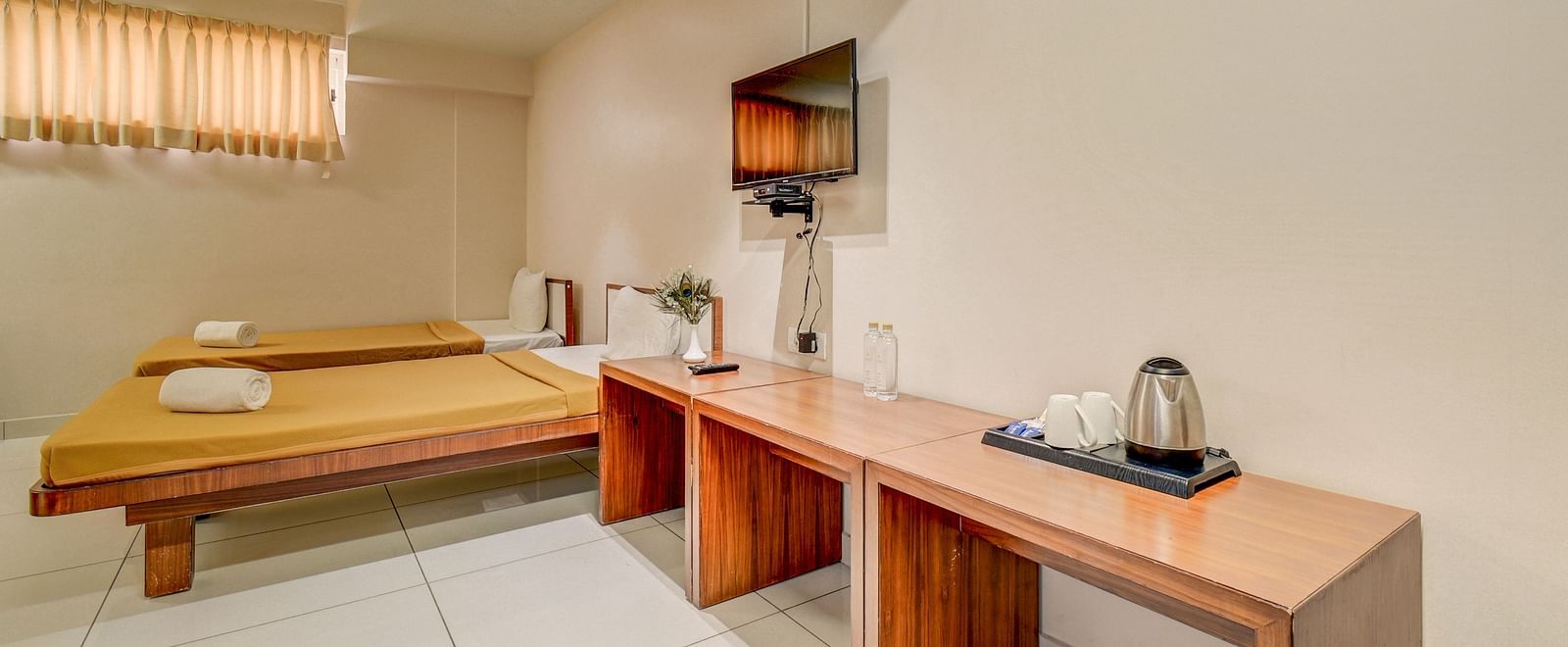 A spacious room at Harigovinda's JNStay, featuring two beds, a wooden table placed against the wall, and a wall-mounted TV above it