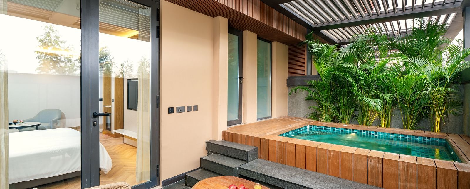 A luxurious villa at Nirvana Luxury Hotel, Ludhiana, features a private plunge pool surrounded by lush greenery, a cosy outdoor seating area with a wooden table, and direct access to the villa's interior.