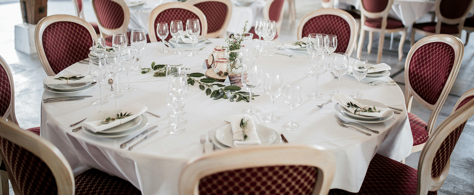 Tables set for a formal event with elegant white tablecloths and red chairs.