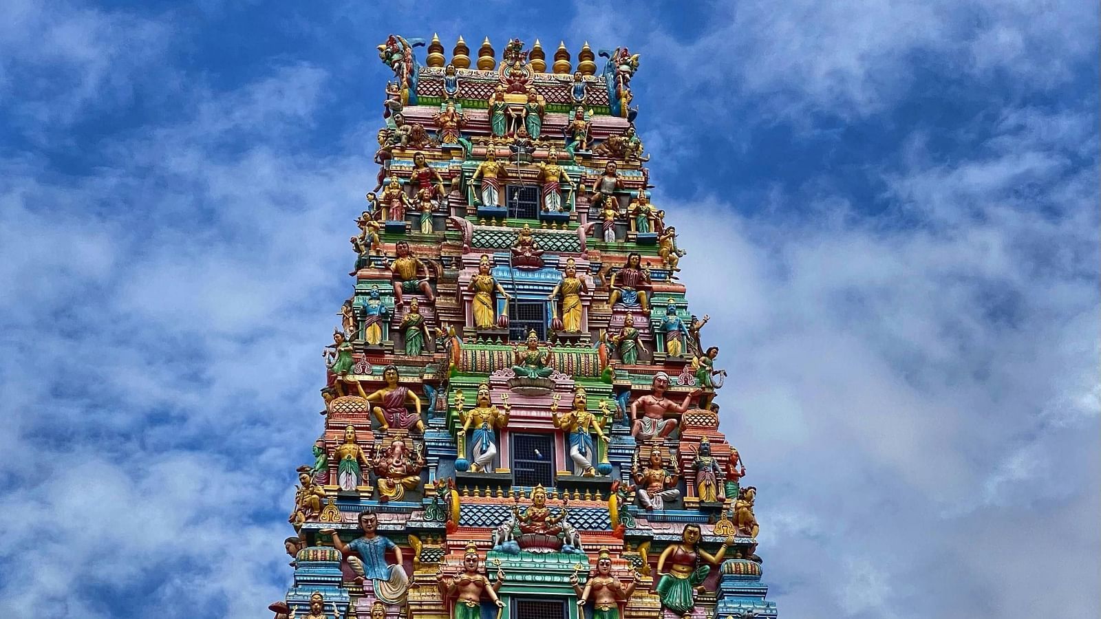 Colourful temple tower with intricate carvings against a clear blue sky.