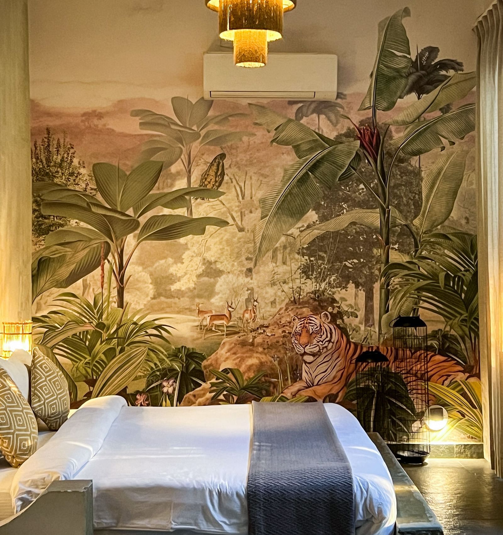 A large bed placed in front of a beautiful wallpaper covered wall and a lamp hanging from the above - Utsav Camp