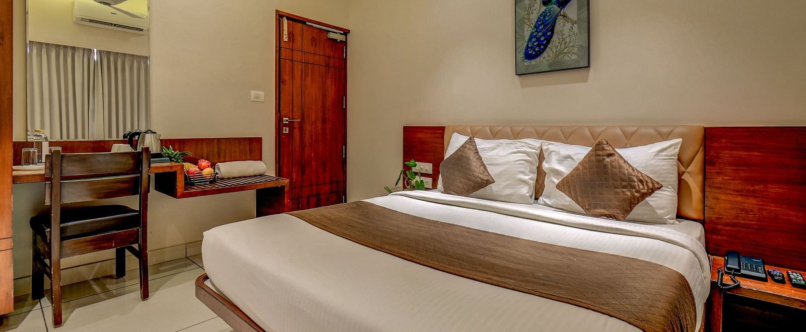A spacious room at Harigovinda's JNStay with a large bed, wooden headboard, bedside table, photo frame above, and a side table with a wall-mounted mirror and chair