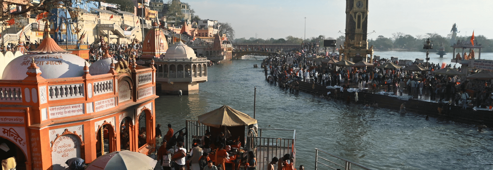 Several people scattered around on the banks of a river during the early morning, featuring a clock tower at a distance.