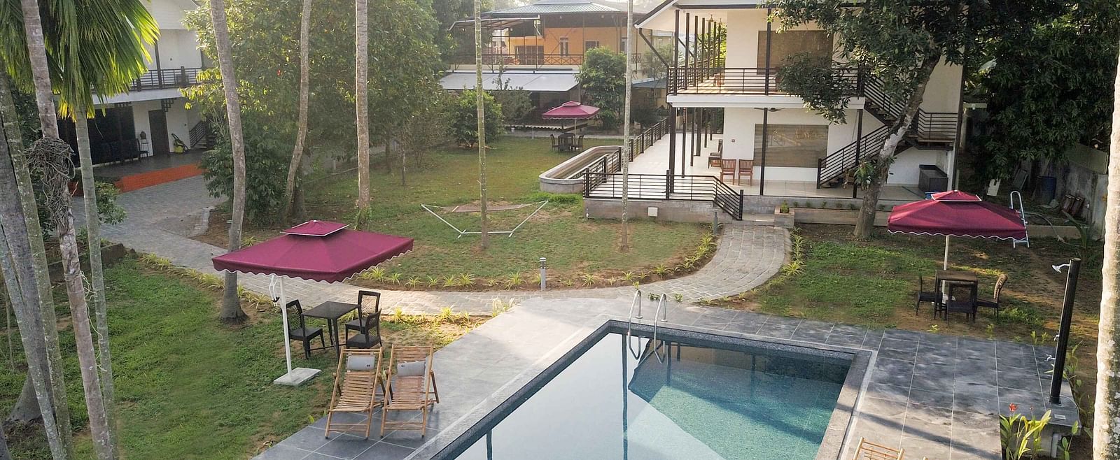 A swimming pool surrounded by lounge chairs and tropical vegetation, with buildings visible in the background.
