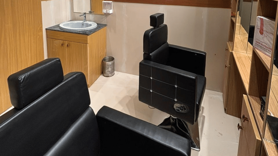 Salon at ABN Sarovar Portico, Jim Corbett featuring two chairs, a shelf with cosmetic products, a sink with mirror, and a storage area at the corner.