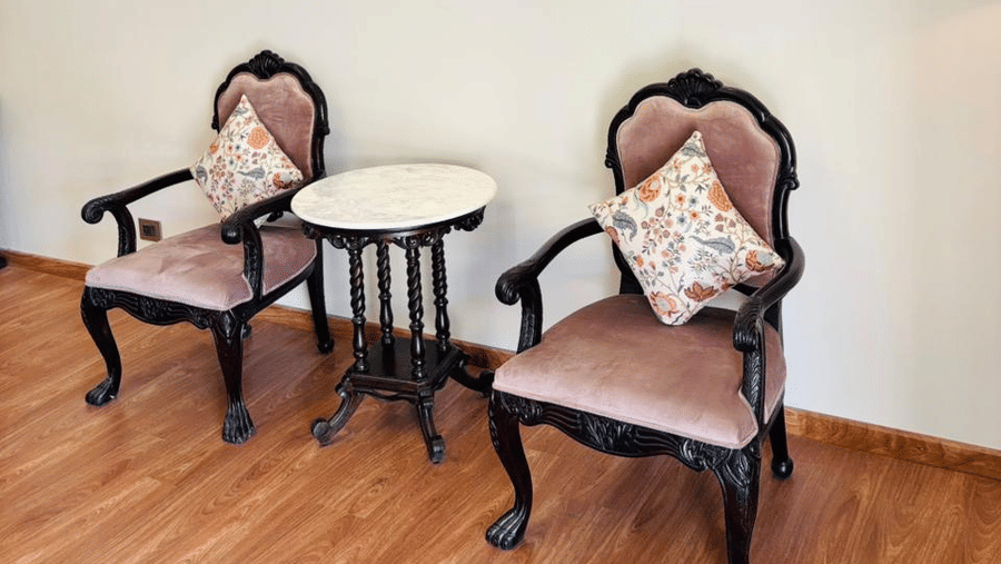 Seating area at Vana Suites featuring two chairs with cushions and a centre table. Above the seating area there are two lit lamps attached to the wall.