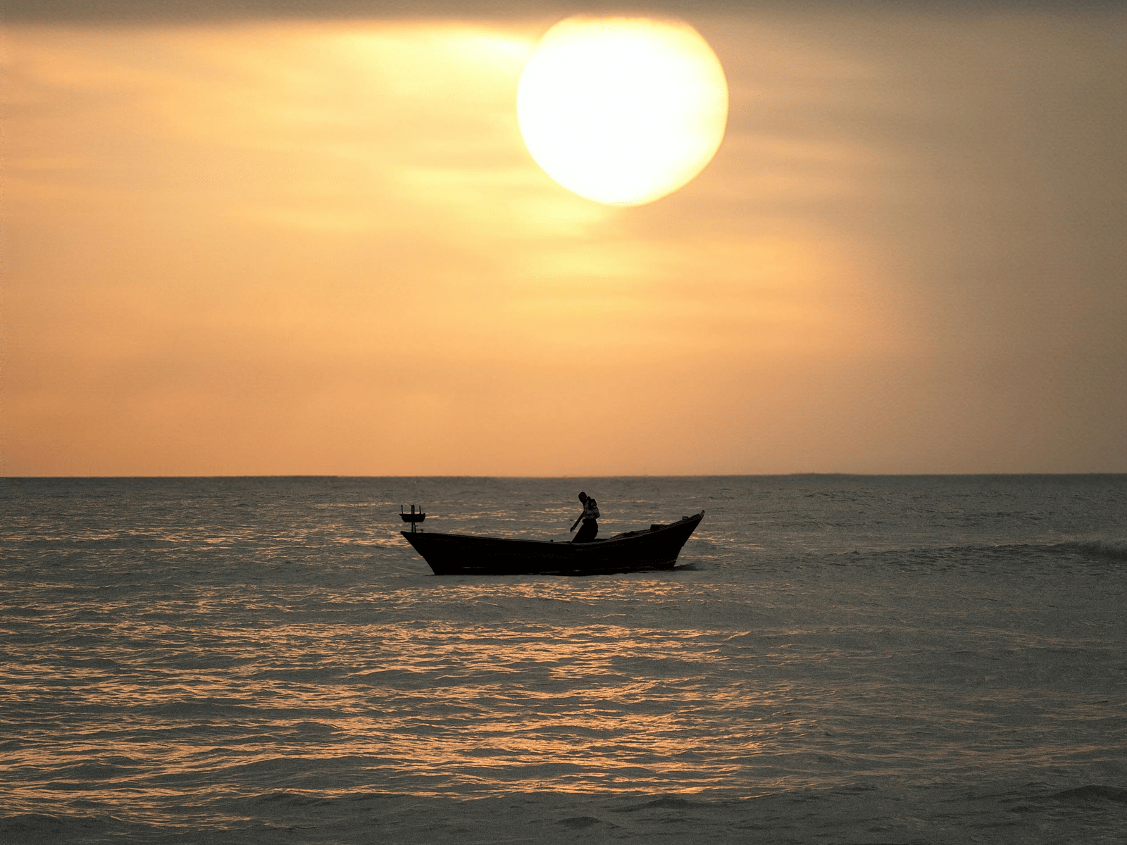 A small boat floating on calm sea water during sunset as the sun reflects softly on the surface creating a serene coastal view.