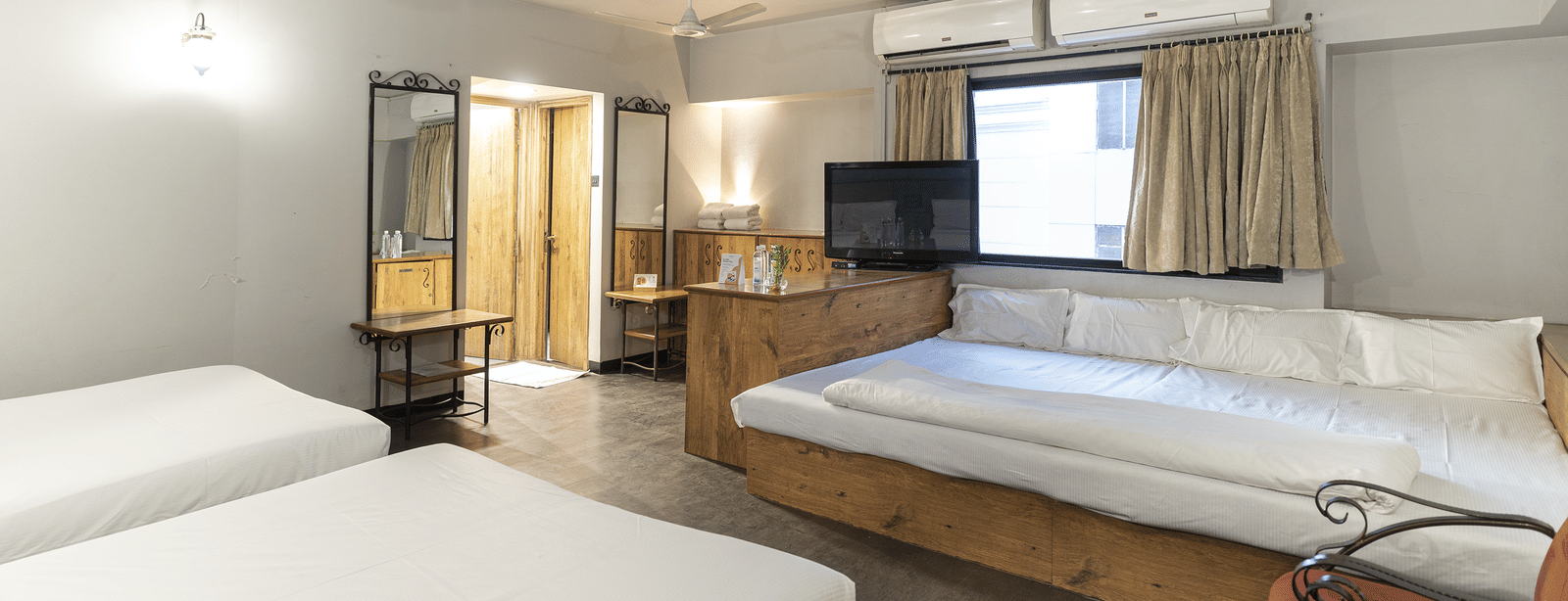 A spacious room with 3 beds, wooden furniture and curtains at Infiniti Hotel, Indore.