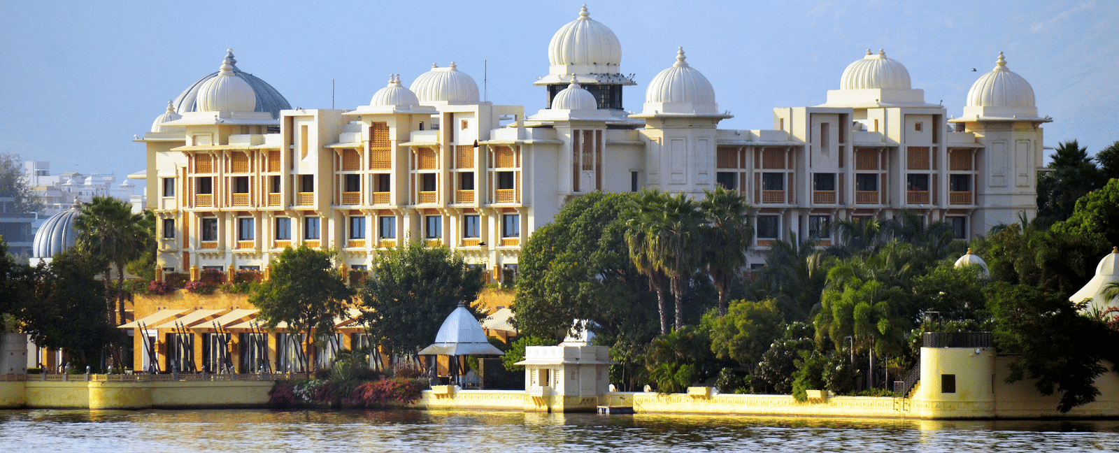 An overview of City Palace in front of Lake Pichola with green trees in front of the building.