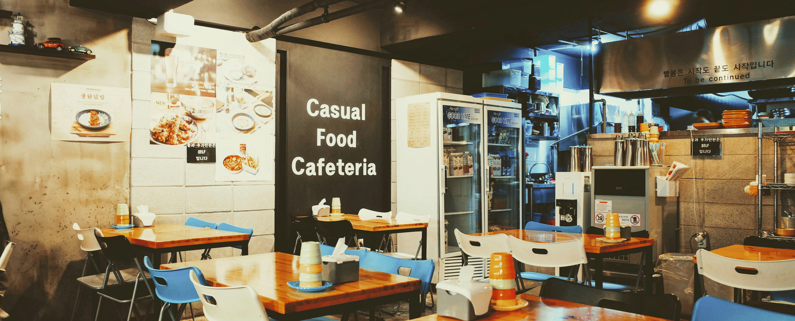 The interior of a modern cafe with tables, chairs, and warm lighting.