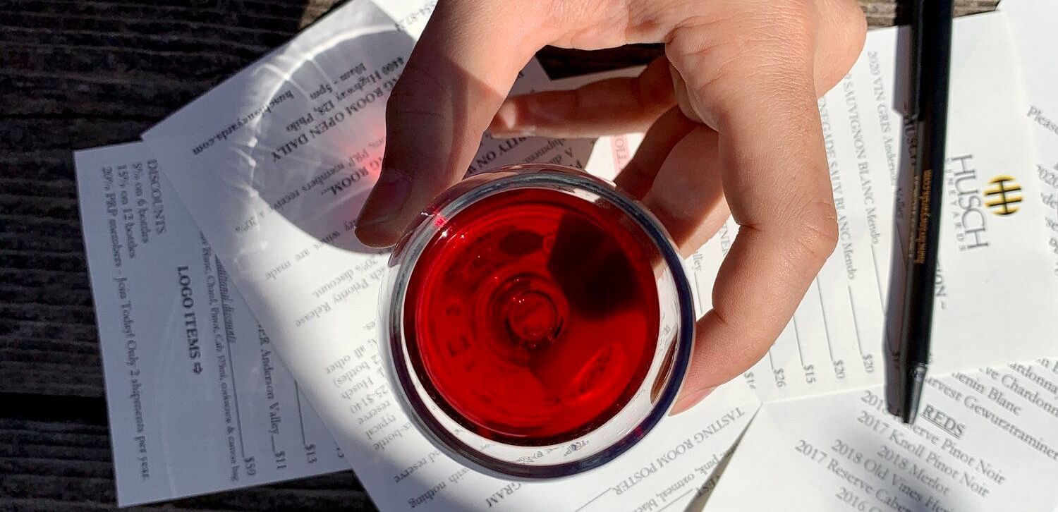 An image of a person holding a glass of wine and there are some papers below it which has Husch written along with other texts