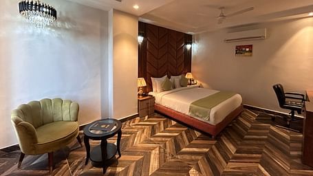 Image of Super Deluxe Room at DLS Grand Luxotica, Dehradun featuring a sitting space including a couch and a coffee table placed at a distance from the plush bed under warm lighting