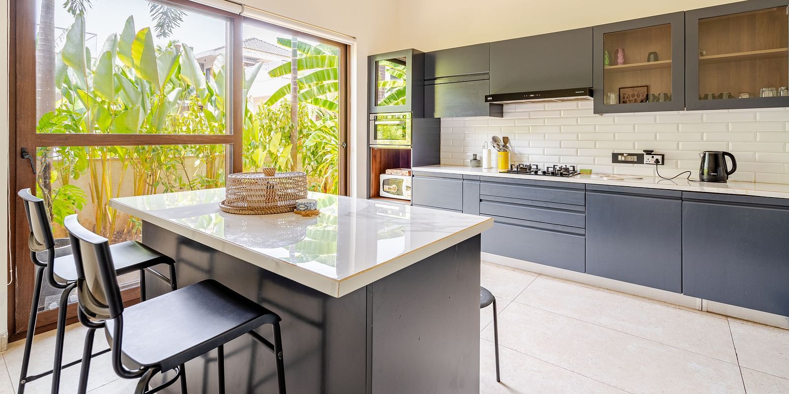 Modern kitchen at Lindsay Manor with a centre island, bar stools, cabinets, microwave, and large windows overlooking greenery.