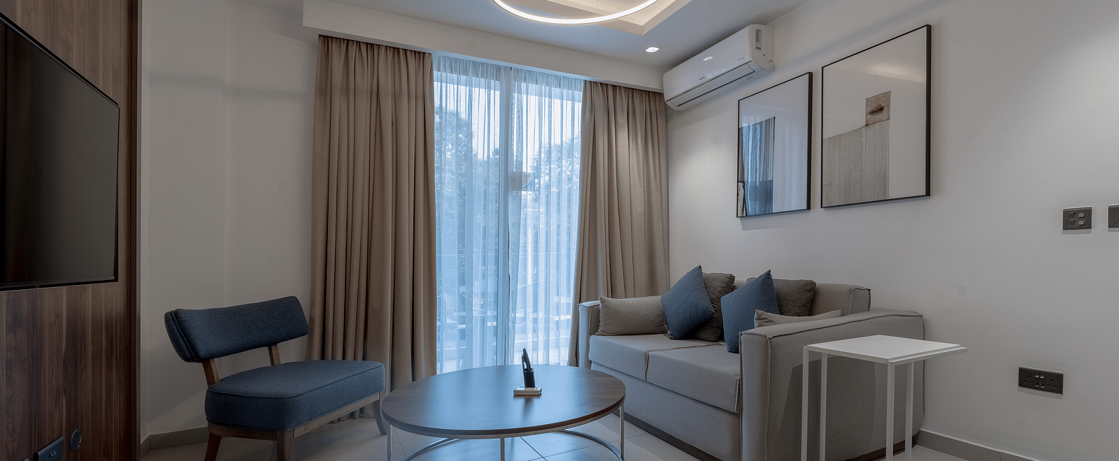 A modern living room in a Premier Suite with stylish furniture, large windows, and elegant decor. - The Pelican Hotel, Accra