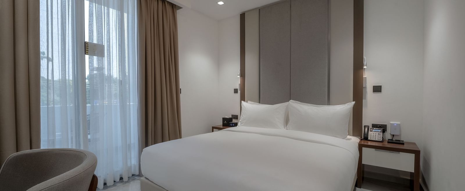 A modern Junior Suite with a large king size bed near a large window. - The Pelican Hotel, Accra