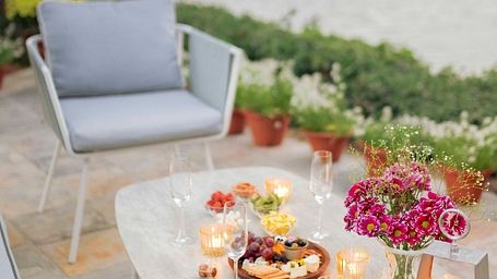 Picturesque table with a romantic setup that includes candles, flowers, wine glasses and plates of food placed on a dock beside a running stream of water - Karma Chalets