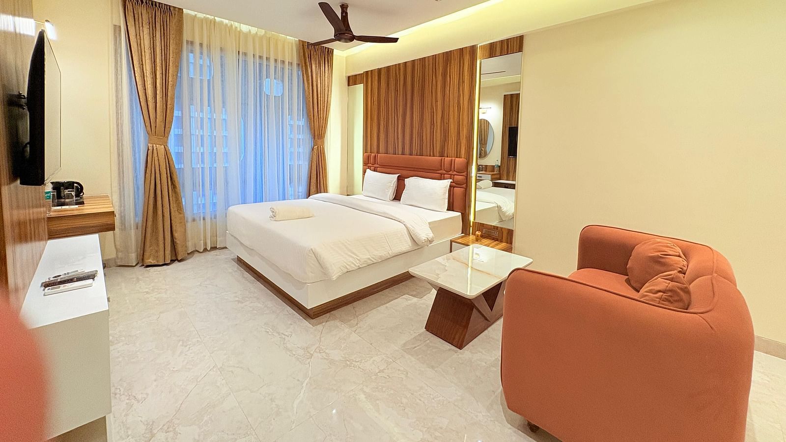 A spacious bedroom featuring a king size bed, a large sofa, and a wall-mounted television at Hotel Mumbai House, Vashi