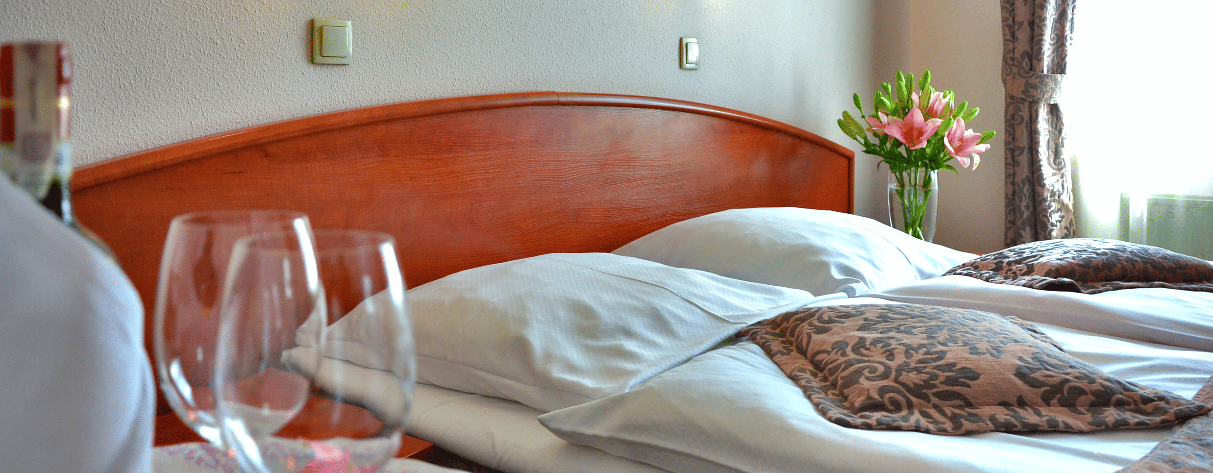 A neatly arranges bed with a person bringing wine bottle and glasses