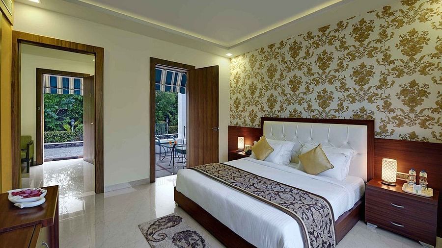 A spacious bedroom at Clarks Safari, Ranthambore, featuring a comfortable bed, a balcony overlooking the surrounding greenery, and elegant decor.