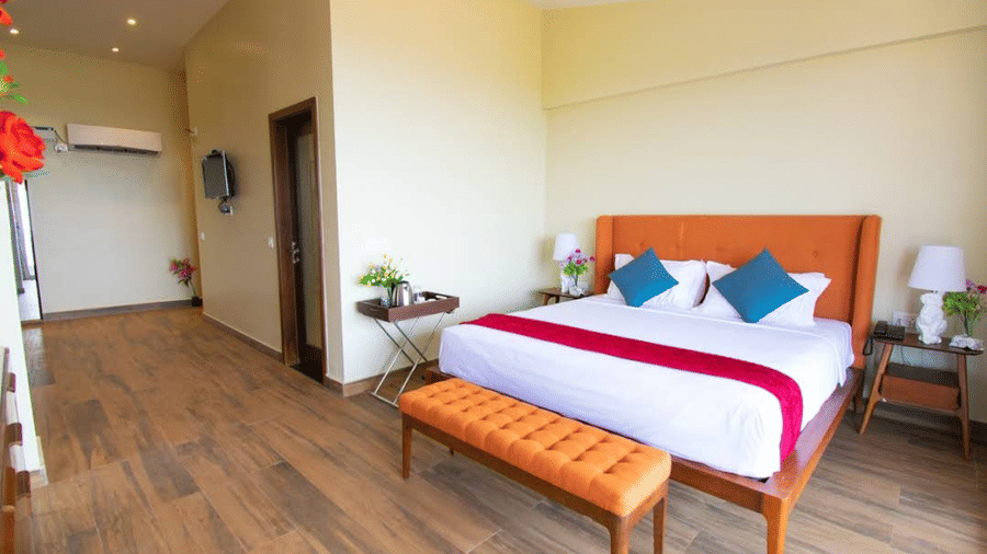 A bedroom with a king size bed, orange headboard, and wooden flooring at Estherea Elite, Morjim.