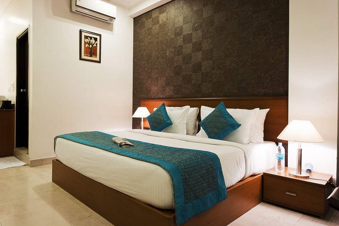 A hotel room featuring a bed with pillows, a textured wall behind the headboard, and bedside tables with lamps - Asian Suites. 