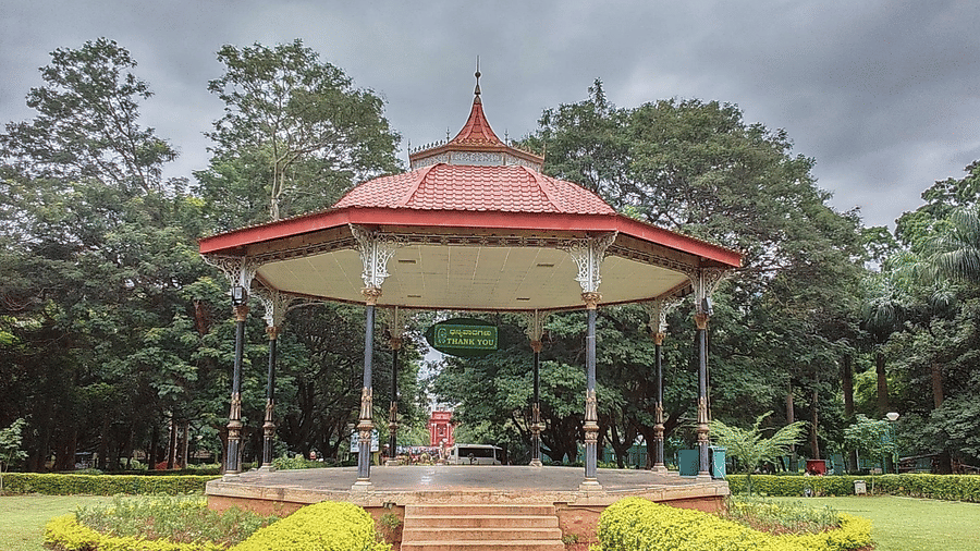 An open pavilion with a red roof surrounded by greenery and a walkway leading to a garden.