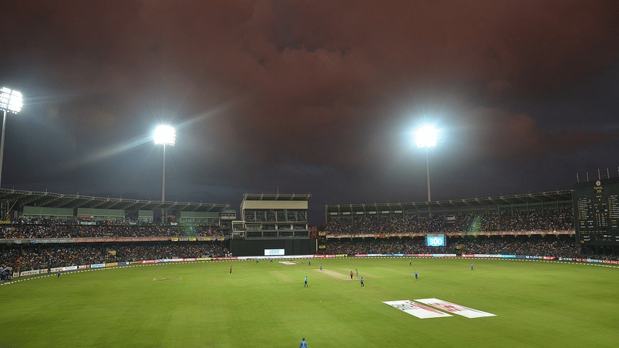 Dramatic night cricket ground under powerful floodlights, with empty pitch and glowing stadium seating ready for the match.