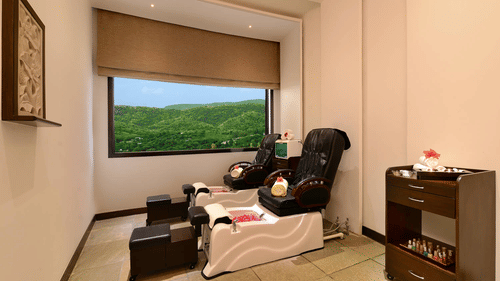 massage chairs with a table on the side and a window view of the greenery outside - Staycation in Udaipur