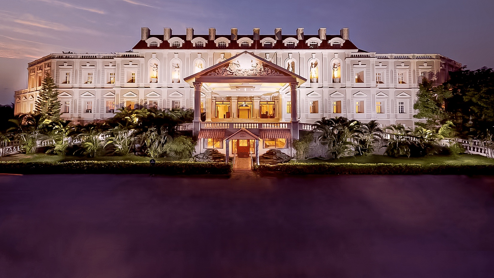 Majestic, brightly lit hotel building at dusk, reflected in a dark body of water - Jenneys Residency, Coimbatore