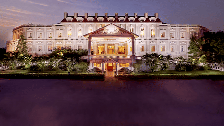Majestic, brightly lit hotel building at dusk, reflected in a dark body of water - Jenneys Residency, Coimbatore