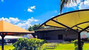 Covered outdoor dining area with tables lined under a beige canopy amidst lush greenery. | Vistar Resort, Bengaluru