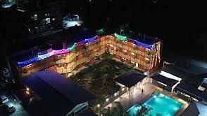 Nighttime view of a brightly lit resort with colourful lights illuminating the façade and surrounding pool. | Vistar Resort, Bengaluru